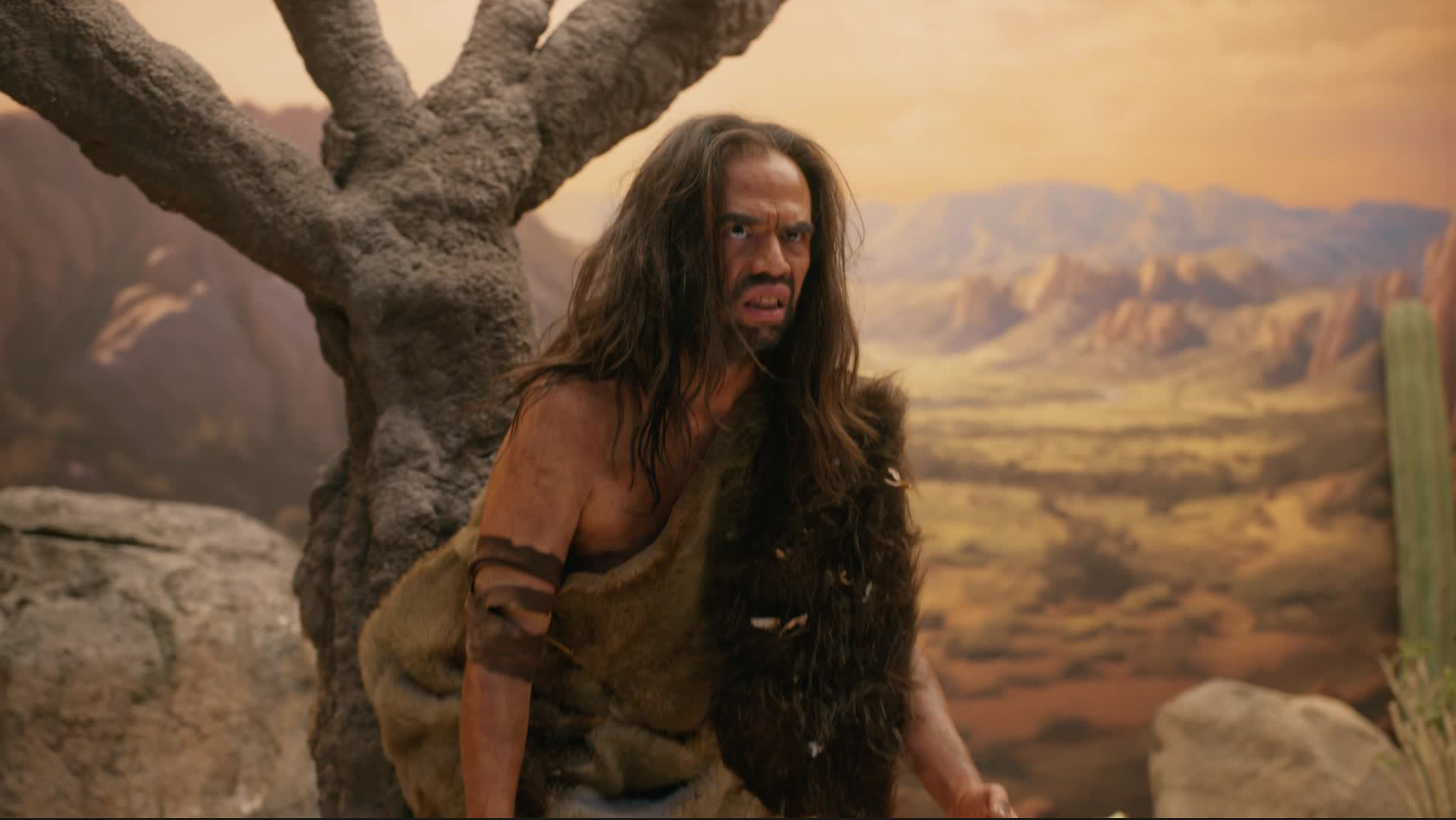 Person in a desert landscape with a tree and mountains in the background